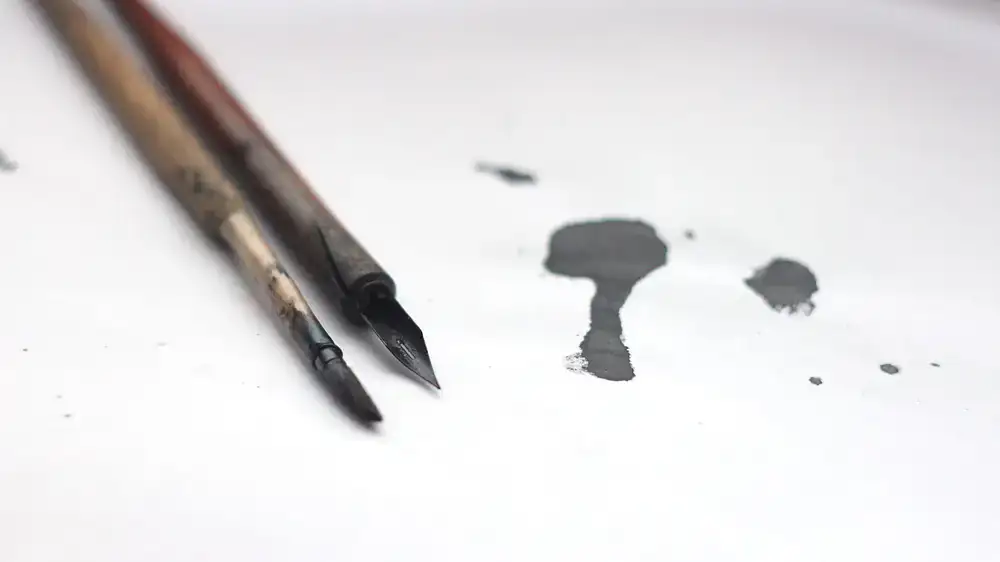 Close up of vintage calligraphy nibs and dark ink resting on textured handmade paper